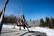 Mother swinging with daughters in big wooden swing in early spring snowy mountains against tiny house and car