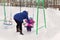 Mother swings her daughter on a swing on a winter afternoon outdoors in the Park