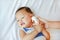 Mother takes temperature for baby boy with ear thermometer on bed at home