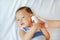 Mother takes temperature for baby boy with ear thermometer on bed at home