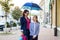 Mother talks with her daughter for ten years on her way to school. Urban background, under an umbrella.