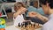 Mother teaching cute boy to play chess while child is having fun moving pieces