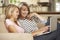 Mother With Teenage Daughter Sitting On Sofa At Home Using Laptop