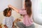 A mother tenderly ties her mixed-race confused daughters hair, both smiling, in a cozy, sunlit room moment of maternal