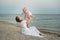 Mother throwing baby up on sandy beach sea background. Seaside holiday with small child