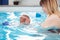 Mother traning her newborn baby to float in swimming pool