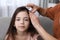 Mother using lice treatment spray on her daughter`s hair indoors