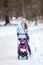 Mother walking with her child on winter park, pulling sledge with daughter on snow pathway