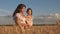 Mother walks with the baby in the field hold spikelets with wheat in hand. little daughter kisses mom on a wheat field
