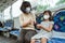 a mother wears a mask and her daughter uses a tissue to clean her hands while sitting