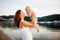 Mother which turns the child against a sunset and water. Happy mom and baby. Playing on beach. Young woman tossing up her son