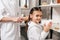 mother in white bathrobe combing daughter hair with wooden hairbrush near shelves