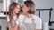 motherhood, loving female parent gently hugs her daughter who eats sweet gingerbread with milk sitting on floor backdrop