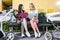 mothers sitting on bench near baby strollers with folder and coffee