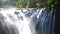 Motion blur of a waterfall and it surrounding mist with tree branches in the foreground. The left side have very strong over