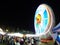 Motion blurred bright neon light ferris wheel on dark evening sky with unidentified crowed moving around