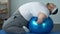 Motivated fat male lifting dumbbells lying on fitness ball, slimming program