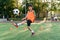 Motivated teen football player stuffs soccer ball on leg. Practicing sport exercises at artificial stadium.