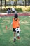 Motivated teen football player stuffs soccer ball on leg. Practicing sport exercises at artificial stadium.