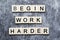 The motivating slogan Begin Work Harder formed with tile letters