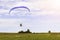 Moto paraglider flying over a field in a blue sky with clouds.
