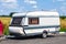 A motor home in the form of a white trailer in a parking lot near the road, secured to the car while traveling in remote