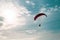 Motor paraglider flying in blue sky with white cloud in background.