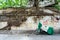 Motorcycle covered with tarpaulin stands on Vietnam street in Ho Chi Minh City, roots of tree crawling over wall