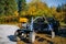 Motorcycle cultivator standing against the trees with green and yellow foliage. Autumn works on the improvement of the territory