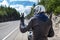 Motorcycle driver rear view at asphalt road, sitting on motorbike and showing victory sign wit hand