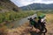 Motorcycle enduro traveler with suitcases standing on a top hill above the river stream