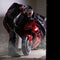 Motorcyclist in full gear and helmet removes the cover from the red sports motorcycle. Dust cover on the motorcycle