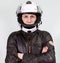 Motorcyclist man wearing moto helmet, leather jacket looking confident at the camera with crossed arms. Grey background