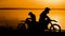 Motorcyclist silhouette at sunset. He freely travels around the sands on the shore of the river.