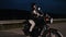 Motorcyclist woman sitting on retro-styled motorcycle. Young female driver in helmet at night on roadway. Trip, freedom