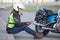 Motorcyclist woman typing a message in her smartphone while sitting on roadside near motorcycle