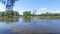 A motorized plastic boat is floating on the river and fishermens are trolling for predatory fish. Willow branches lean over the wa