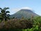 Mount Arenal in Costa Rica. Picturesque landscape, clouds cover the top of the mountain, around flowers, palm trees.