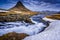 Mount Kirkjufell towers over rushing waterfalls in Iceland.