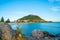 Mount Maunganui, popular travel and holiday destination with landmark mountain beyong long white beach and rocky foreground