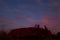 Mount Uluru at night. Stars in the sky and pink clouds. Eroded rock, orange color. Low bushes in front. Northern Territory NT,