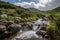 mountain biker riding past rushing stream, with view of the valley beyond