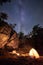 Mountain campsite at night amid huge steep rock formation. Tourist tent lit by burning campfire