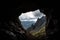 mountain cave, with view of the open skies, surrounded by clouds and silhouettes of distant peaks