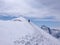 Mountain climber hiking along a long snow ridge on his way to a high alpine summit with tracks in the foreground