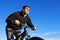 Mountain cyclist portrait, bicyclist in black jacket with mountain bike, blue sky on background, bottom view.