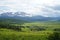 Mountain dale with green gress field under cloudly sky and mountains