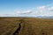 A mountain field with a very long crack going toward the horizon, beneath a deep blue sky with white clouds