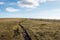 A mountain field with a very long crack going toward the horizon, beneath a deep blue sky with white clouds