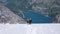 Mountain guide with two clients descending a steep white glacier with a fantastic blue mountain lake far below